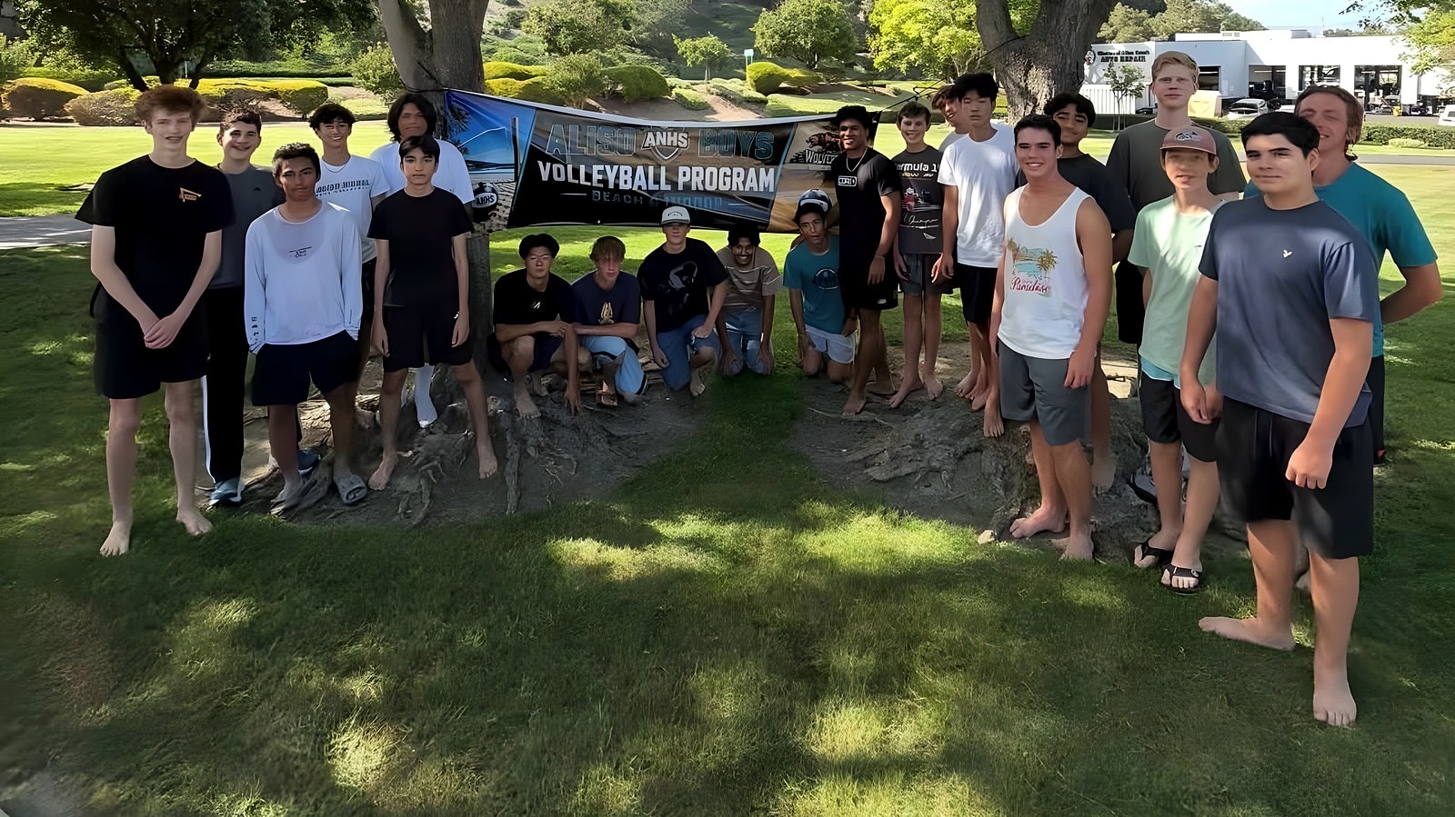 The whole program gathered under a tree with the Aliso Boys Volleyball banner at the beach kickoff