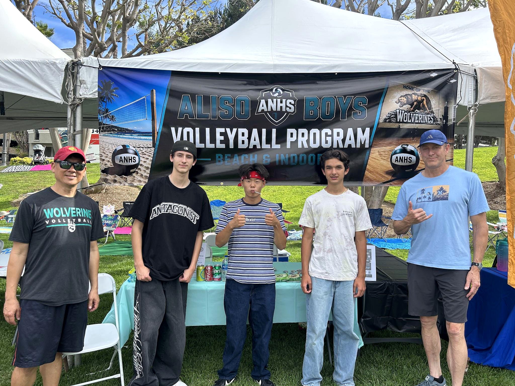 Players and parents under the program tent with the Aliso Boys Volleyball banner at a community event