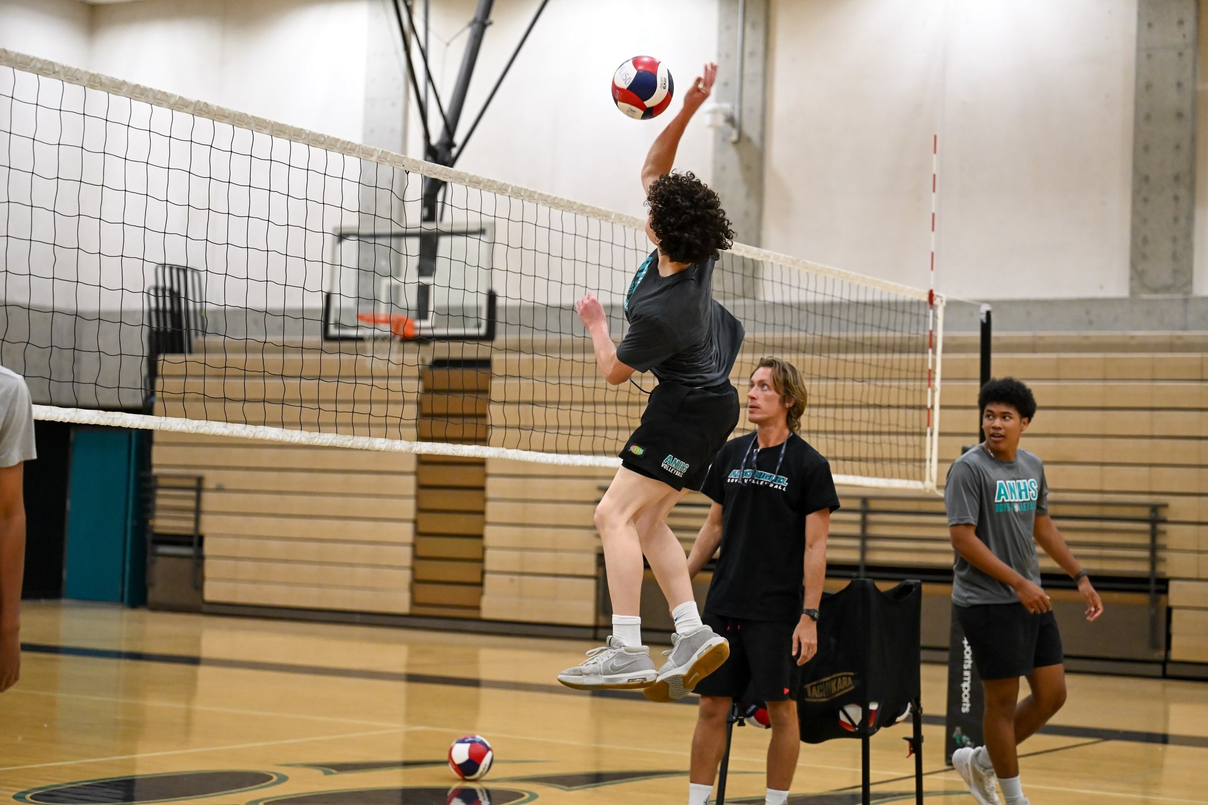 A player hits over the net while teammates look on