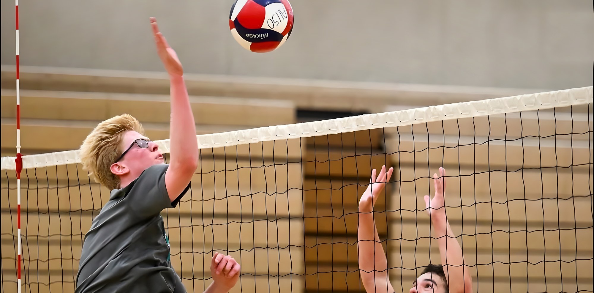 A Wolverine hitter swings over the net against two blockers
